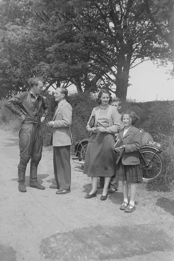 A rider talks to another man stood by their motorcyle, a woman and two children stand close by
